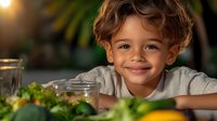 Mixed race boy with curly hair smiling at camera while leaning on kitchen counter with fresh vegetables and glass containers, promoting healthy eating habits and lifestyle.