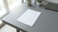 Clean minimalist workspace with blank white paper on gray desk near window with natural light for mockup and branding projects.