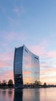 Modern curved glass office tower reflecting sunset colors over calm waterfront, showcasing contemporary architecture and urban development for corporate, real estate, and business design projects.