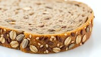 Artisan whole grain bread slice with mixed seeds and nuts on white background isolated for healthy food design projects and culinary presentations.