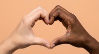 Two diverse hands forming heart shape symbol representing love unity and racial harmony against warm peach background for social campaigns.