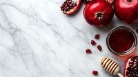 Fresh red pomegranate and apple with honey dipper on white marble background. Healthy organic fruits and juice in glass jar, flat lay composition with copy space.