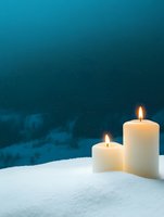 Glowing white candles on snow against dark turquoise winter night sky, creating peaceful atmospheric mood for holiday season and spiritual contemplation.