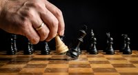 Strategic chess move with hand positioning white king piece on wooden chessboard against black pieces in competitive game setting for business concepts.