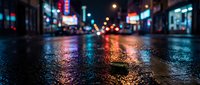 Wet urban street at night with colorful neon lights reflecting on pavement, bokeh city buildings and signs blurred in background for nightlife and metropolitan concepts.