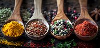 Aromatic spices and peppercorns in wooden spoons, including turmeric, red chili powder and mixed colorful peppercorns on dark background with herbs.