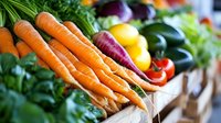 Fresh organic carrots with green tops displayed at farmers market alongside colorful vegetables including peppers and leafy greens for healthy cooking and nutrition.
