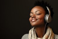 Young African American woman with closed eyes and bright smile wearing headphones and cozy scarf against dark background, expressing joy while listening to music.