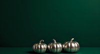 Metallic gold pumpkins arranged on deep teal surface against matching background, suitable for autumn, fall, and holiday seasonal design projects and decorations.