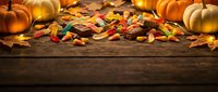Autumn harvest scene with colorful candy corn scattered on rustic wooden table surrounded by orange pumpkins and golden maple leaves for seasonal celebrations.