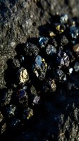 Macro shot of pyrite mineral crystals with metallic luster scattered on dark rocky surface, showcasing golden and blue iridescent reflections for geology and mineral collection content.