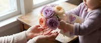 Woman giving beautiful bouquet of purple and peach roses to another person in cozy indoor setting. Perfect for Mother's Day, Valentine's Day, gifts, celebrations.