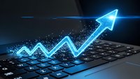 Glowing blue digital arrow emerging from laptop keyboard showing upward growth trend with particle effects for business success concepts.