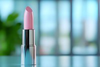Elegant pink lipstick in silver metallic case against soft blurred background with natural window light and greenery, showcasing luxury cosmetic product.