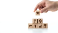 Hand placing wooden cube with graduation cap icon on pyramid of education blocks with academic symbols on white background for learning concepts.