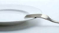 Silver fork resting on a white ceramic plate, minimalist dining concept on light background, symbolizing meal preparation or hunger.