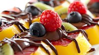 Fresh tropical fruit dessert with dark chocolate drizzle, raspberries, blueberries and kiwi pieces arranged in appetizing composition. Sweet gourmet food styling.