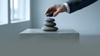 Businessman in dark suit placing smooth stone on balanced stack, symbolizing stability, growth, and business success in minimalist office setting.