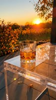 Glass of whiskey with ice on table overlooking autumn vineyard at golden hour sunset, suitable for beverage, lifestyle, and travel photography.