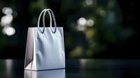 White paper shopping bag with handles on dark surface against blurred green bokeh background for retail and commercial use.