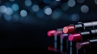 Luxurious lipsticks arranged on dark background with blue bokeh lights, showing vibrant red and pink shades in elegant black tubes. Professional cosmetics setup.