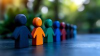 Colorful wooden figures standing in line on blue surface with blurred background, representing diversity, teamwork and social inclusion in business concept.