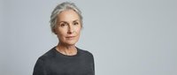 Mature woman with gray hair and fair complexion wearing dark gray sweater against neutral background, suitable for healthcare, wellness, and corporate communications.