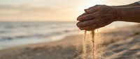 Hand pouring sand at sunset beach, symbolizing time passage and relaxation. Suitable for wellness, mindfulness, and lifestyle content.