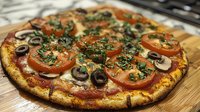 Homemade vegetarian pizza with fresh tomatoes, mushrooms, olives and herbs on wooden cutting board ready to serve for dinner or lunch meal.