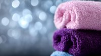 Rolled pink and purple towels stacked together with soft bokeh background, suitable for spa, wellness, hospitality and bathroom product marketing.