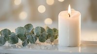 White candle burning beside eucalyptus branch and sea salt crystals creating peaceful spa atmosphere with soft bokeh lights in background.