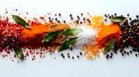 Vibrant spices scattered on white surface with fresh bay leaves creating dynamic composition of red paprika, turmeric powder and black peppercorns in line pattern.