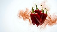 Fresh red chili peppers with vibrant spice powder explosion on white background, capturing bold heat and flavor for food and culinary concepts.
