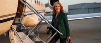 Professional businesswoman in green blazer boarding private jet at airport terminal during golden hour sunset for luxury corporate travel.
