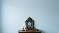 Ornate vintage mirror with ghostly apparition reflection on wooden shelf with candles and decorative items for gothic, supernatural, or Halloween-themed designs.