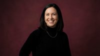 Happy young Hispanic woman in black turtleneck sweater smiling warmly against burgundy background for professional headshot and portrait photography.