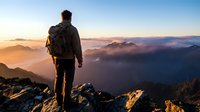 Hiker with backpack standing on mountain peak at sunrise overlooking misty valley landscape, adventure travel and outdoor exploration concept for hiking and trekking campaigns.