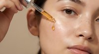 Young Asian woman applying golden facial serum with dropper for skincare routine and anti-aging treatment on glowing healthy skin.