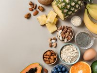 Healthy food composition with tropical fruits, nuts, seeds, oats and egg on neutral background for balanced nutrition.