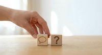 Hand placing wooden cube with speech bubble next to question mark block on table representing communication, inquiry and problem-solving concepts.