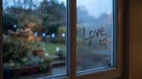 Word Love and heart drawn on a foggy rainy window with blurred garden view, romantic moody atmosphere on a cold day.