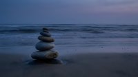 Balanced stone stack on serene beach at twilight with gentle waves and purple sky creating peaceful meditation atmosphere for wellness concepts.