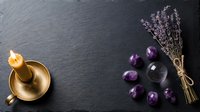 Spa wellness composition with brass singing bowl, dried lavender bundle and purple amethyst crystals on dark slate background for meditation and relaxation.