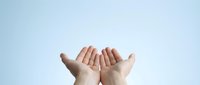 Open cupped hands reaching upward against soft blue background suggesting prayer, hope, receiving blessings or offering help in spiritual moment.