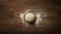 Fresh raw dough ball sprinkled with flour on rustic wooden table background, top view. Traditional bread making process captured from above.