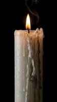 Burning white candle with melted wax dripping down sides and smoke rising from flame against black background for atmospheric lighting concepts.