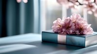 Pink cherry blossom flowers lying on hardcover book with teal blue cover in soft natural window light creating romantic spring atmosphere.