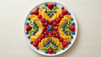 Colorful fruit platter arranged in symmetrical pattern on white plate with strawberries, blueberries, kiwi and pineapple for healthy eating and catering.