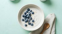 Creamy yogurt bowl topped with fresh blueberries and wooden spoon on mint green surface, perfect for food blogs, healthy eating content, breakfast recipes, and wellness marketing.