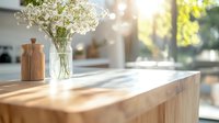 Sunlit wooden kitchen counter with glass vase of delicate white flowers and wooden pepper mill, morning light casting soft shadows through window, creating cozy home atmosphere.